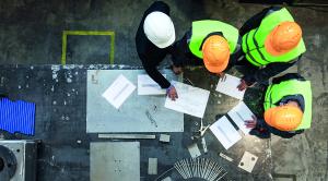 Workers and manager in safety helmets working with documents at factory table