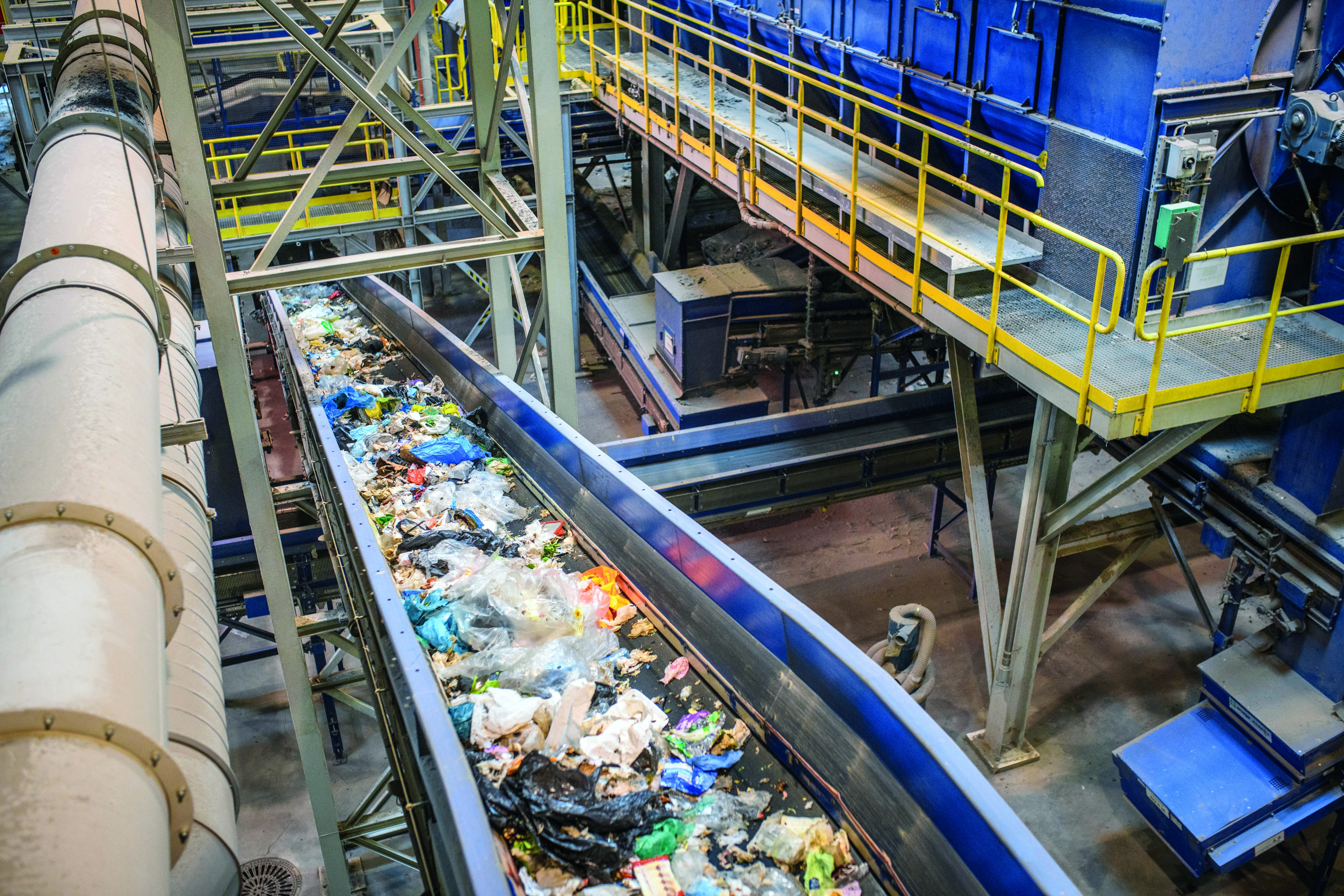 High angle close-up of pieces of recyclable garbage on conveyor belt inside waste management facility.